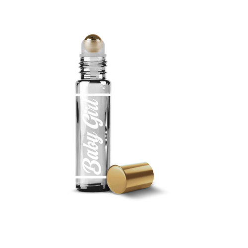 A clear glass roller bottle with a gold metallic cap and a gold ball applicator, shown on a white background with the cap placed beside it. The bottle has a white script label reading 'Baby Gem'.
